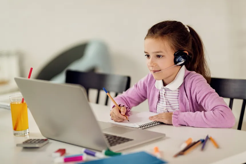 A girl taking notes while learning on a laptop at home